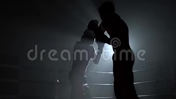 两个戴着头盔和拳击手套的人在黑暗中在擂台上战斗慢动作剪影视频的预览图