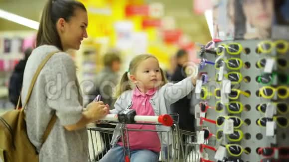 超市里幸福家庭的画像年轻的母亲和小女儿为女孩儿挑选太阳镜视频的预览图