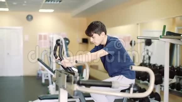 这个年轻人骑着运动自行车训练一个15岁的家伙在健身房训练助听器视频的预览图