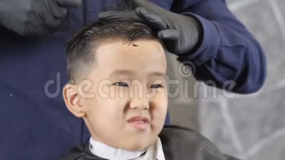 戴着黑手套的理发师在一个亚洲孩子的皇冠上剪了头发男孩震惊了60英尺视频的预览图