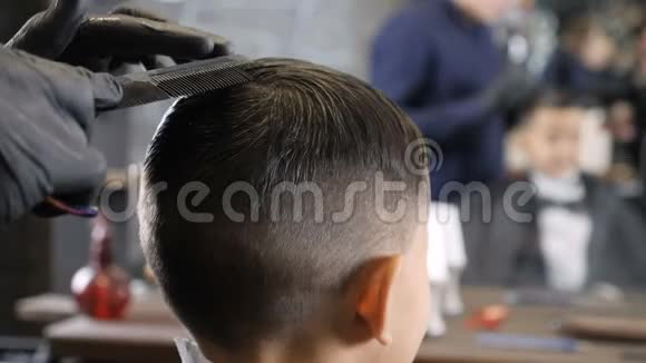 戴着黑色手套的理发师梳理一个亚洲孩子的头发准备给他们剪60英尺长的头发视频的预览图