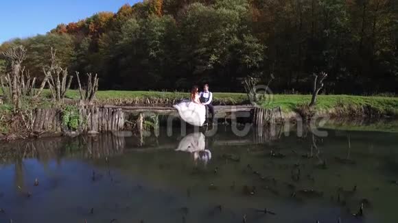 新娘坐在公园的一座小桥上靠近湖边视频的预览图