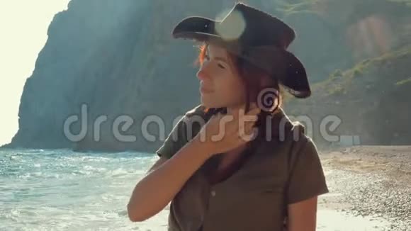 一个美丽的红发旅行女孩戴着牛仔帽在海边的肖像视频的预览图