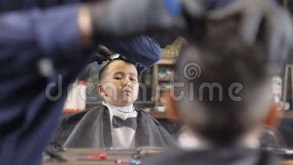 戴黑手套的理发师用剃刀在一个亚洲孩子的头上刮胡子焦点每秒改变60帧视频的预览图