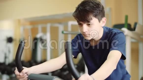 一个15岁的家伙在健身房训练助听器这个年轻人骑着运动自行车训练视频的预览图