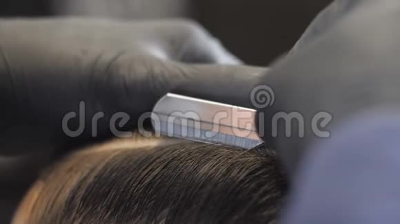 戴着黑手套的理发师用一把直剃刀在一个亚洲孩子的头上剃掉了离别的头发收了60英尺高视频的预览图