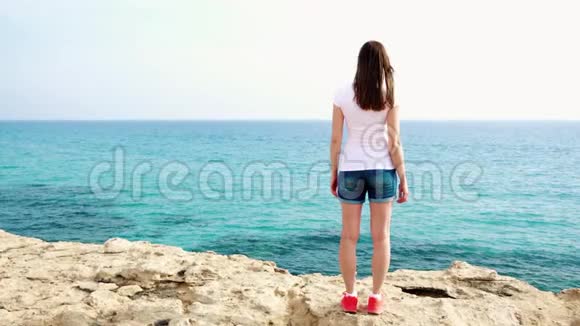 女人在碧海的峭壁上举起双臂女旅行者缓慢地伸出双手视频的预览图