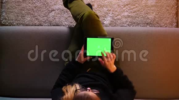 美丽的女孩特写镜头在室内舒适地坐在沙发上用绿色屏幕的平板电脑视频的预览图
