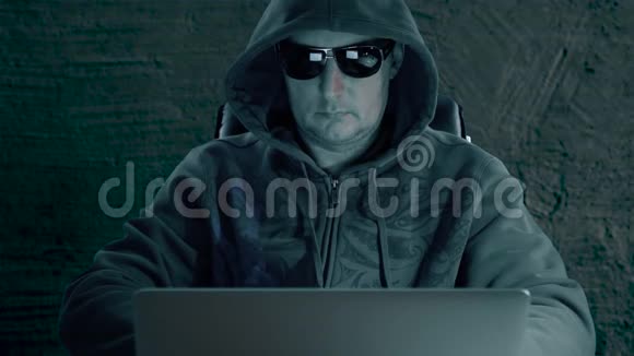 黑客使用手机戴着头巾和眼镜的成年男子坐在笔记本电脑的黑暗夜晚男人用智能手机现代视频的预览图