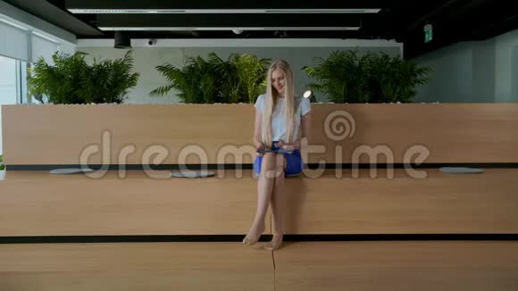 办公室里有平板电脑的放松女人年轻优雅的女人光着脚坐在现代办公室的木制论坛上视频的预览图
