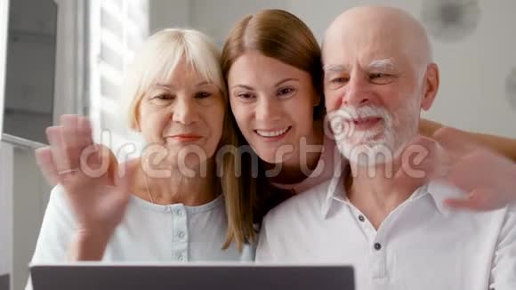 年长夫妇和他们的女儿坐在家里通过信使Skype聊天微笑着挥手视频的预览图