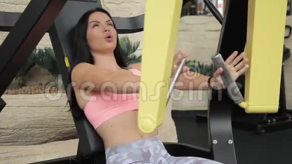 美丽的女人在模拟器上用力地泵她的手的肌肉视频的预览图
