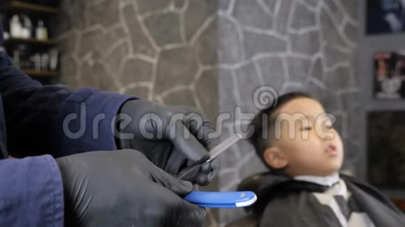 戴着黑色手套的理发师正准备剃一个亚洲小孩60英尺高的直剃须刀视频的预览图