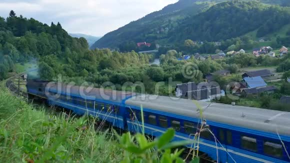 一列蓝色火车在喀尔巴阡山脉经过村庄夏季视频的预览图