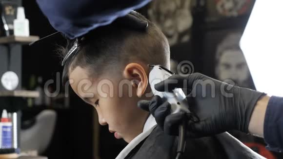 戴着黑色手套的理发师轻轻地剃掉一个亚洲孩子耳朵后面的头发侧视60英尺视频的预览图