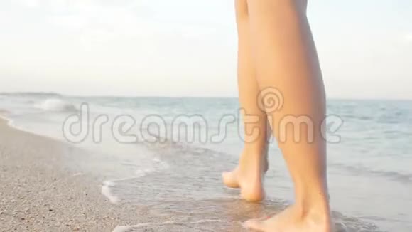 站在海边金色沙滩上的年轻女子的角度女性的腿在海洋附近行走赤脚的女孩继续视频的预览图