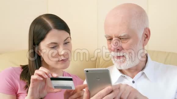 父亲和女儿在智能手机上用信用卡在线购物老年人使用技术视频的预览图