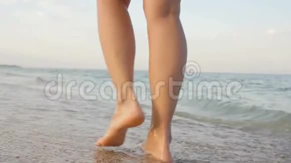 站在海边金色沙滩上的年轻女子的角度女性的腿在海洋附近行走赤脚的女孩继续视频的预览图