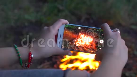 那个女人用电话露营视频拍摄了明亮的篝火视频的预览图