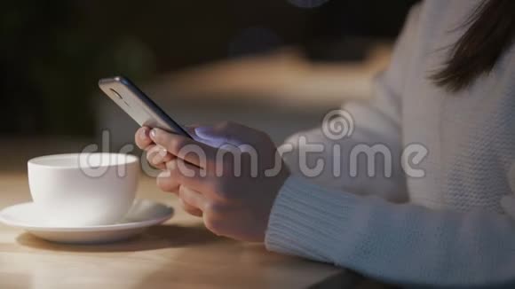 女人在智能手机上滚动页面晚上坐在舒适的咖啡馆里视频的预览图