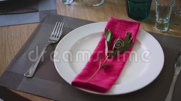 一个盘子四周是酒杯和酒杯的餐具上面放着一张带绿色树枝的粉红色餐巾视频的预览图