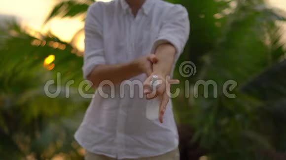 一个年轻人用防蚊剂喷在皮肤上的超慢镜头热带背景视频的预览图