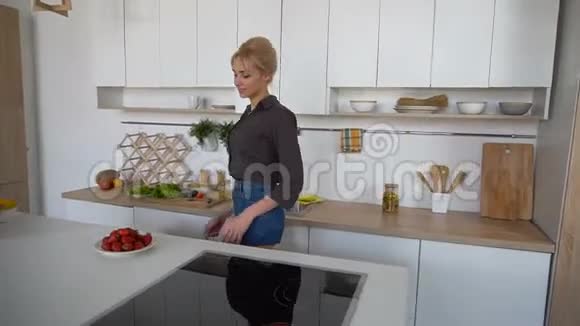 迷人的女孩休息和享受草莓的味道散步和坐在椅子后的厨房表面在现代厨房视频的预览图