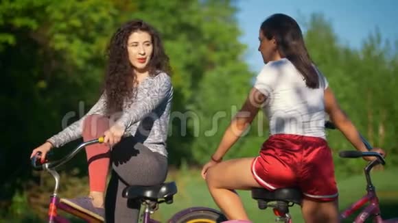 在阳光明媚的夏日两位年轻的骑自行车的人在公园骑自行车旅行中交流和欢笑视频的预览图
