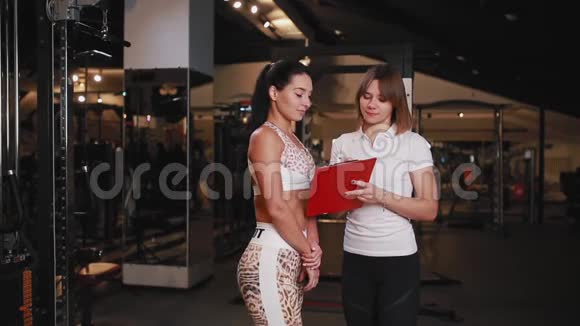 女私人教练在健身房和一个女客户交谈用平板电脑做笔记视频的预览图