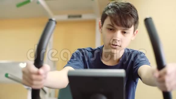 一个15岁的家伙在健身房训练助听器这个年轻人骑着运动自行车训练视频的预览图