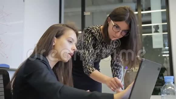 在办公室里两个女人在笔记本电脑前讨论工作问题视频的预览图