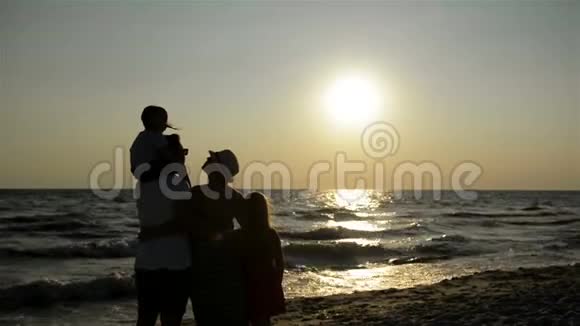两个女儿的父母的黑暗剪影看着海边的日落视频的预览图