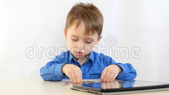 小男孩坐在一张桌子旁用手玩硬币背景是白色的视频的预览图