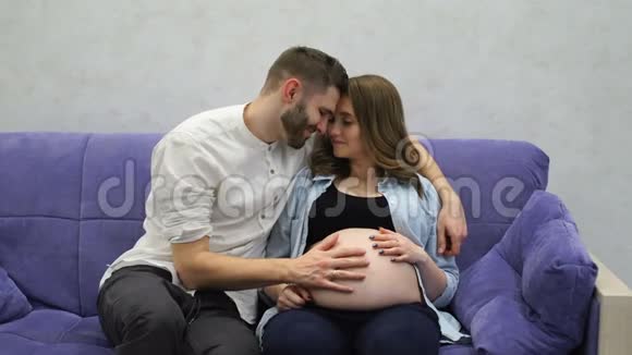 孕妇和丈夫坐在沙发上看电视一个男人和妻子交流视频的预览图