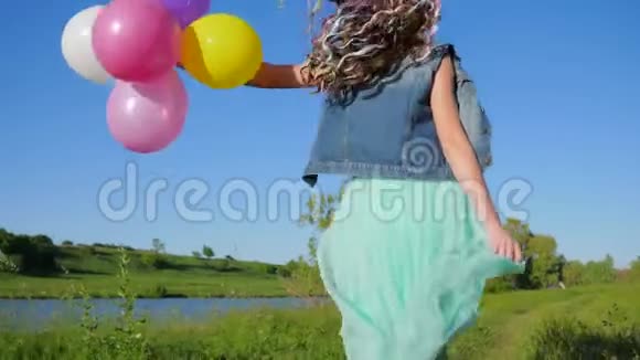 快乐的假期少女头发上有彩色的卡尼卡龙手中有气球在湖边跳跃着大自然视频的预览图