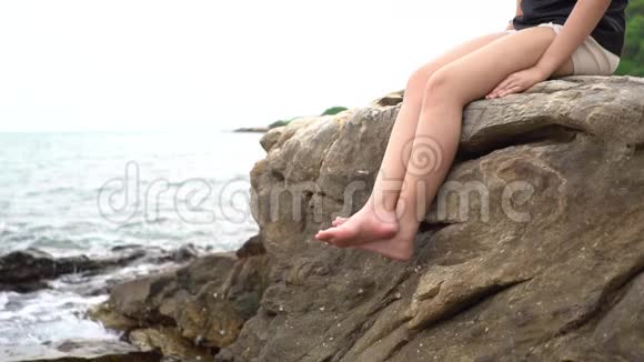动作缓慢2530岁的亚洲女孩穿着黑色西装坐在有海景的悬崖上感觉舒服关系视频的预览图