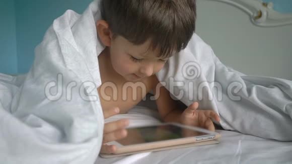 毯子下面的床上放着平板电脑的小男孩视频的预览图