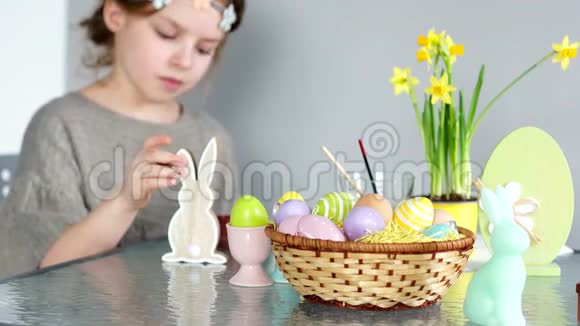 美丽的女孩画了复活节兔子的身影桌子上有颜料一个装有复活节彩蛋的篮子和一个视频的预览图