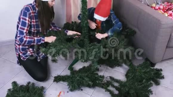 妈妈和儿子戴着圣诞帽在家里安装圣诞树为圣诞节做准备视频的预览图