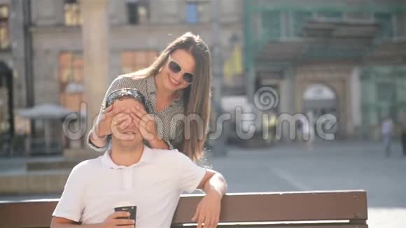 在阳光明媚的城市广场上坐在长凳上的男朋友戴着太阳镜的漂亮女人闭上了眼睛视频的预览图