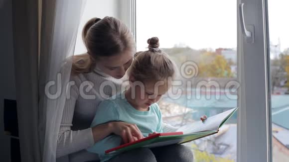 年轻的母亲和女儿在窗户附近看书视频的预览图