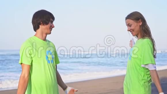 快乐的年轻志愿者穿着绿色t恤衫在海滩上进行图像回收向镜头致意视频的预览图