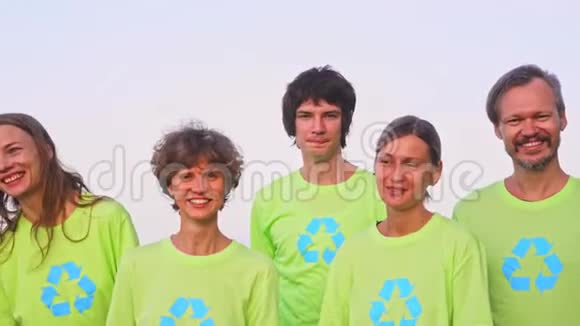 5名年轻志愿者身穿绿色t恤衫将图像回收在海洋海滩上收集垃圾然后在相机上摆姿势视频的预览图