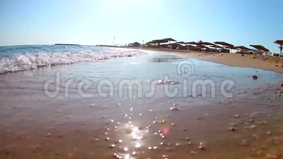 阳光明媚的一天海浪拍打着沙滩上的海浪带着草的沙滩伞红海从下面可以看到广阔的视角视频的预览图