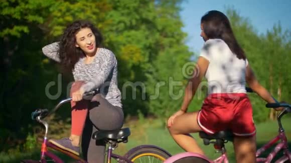 在阳光明媚的夏日两位年轻的骑自行车的人在公园骑自行车旅行中交流和欢笑视频的预览图