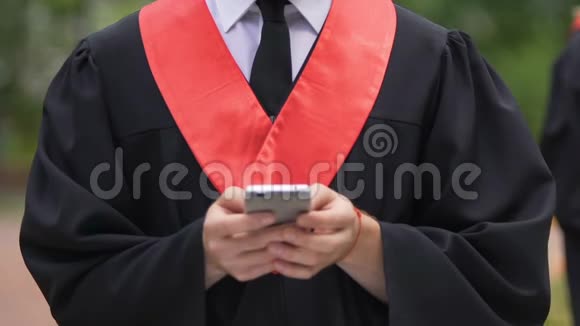 穿着学术服装的男人手在智能手机上打字在线聊天视频的预览图