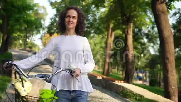 一个穿着白色T恤和蓝色牛仔裤的年轻女子手里拿着自行车车把篮子里放着鲜花视频的预览图