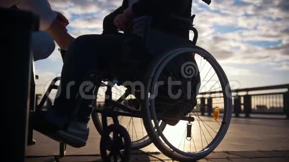 残疾男子坐轮椅在户外日落时说话的年轻女子剪影视频的预览图