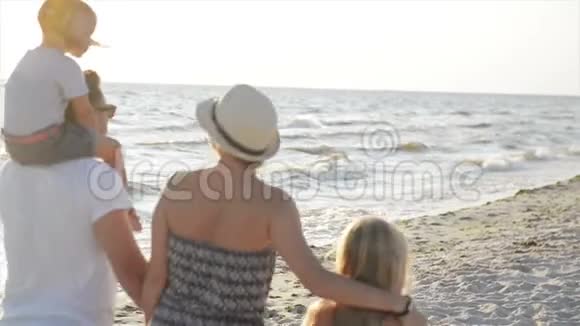两个小妹妹和快乐的母亲和父亲在海滩上牵手散步的后景视频的预览图