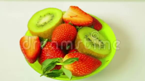 鲜奇异果和切片草莓在蓝色背景上的盘子旋转成一个圆圈从上面看视频的预览图